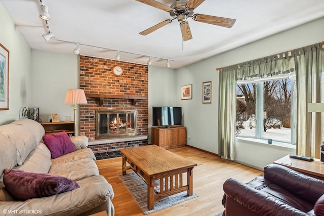 living area featuring a ceiling fan, a brick fireplace, wood finished floors, and baseboards