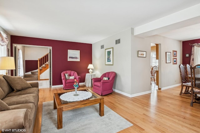 living room featuring light wood finished floors, visible vents, stairway, and baseboards