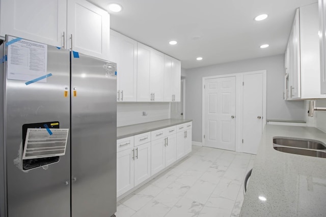 kitchen with light stone counters, white cabinets, stainless steel refrigerator, backsplash, and sink