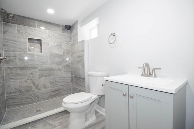 bathroom with toilet, a tile shower, and vanity