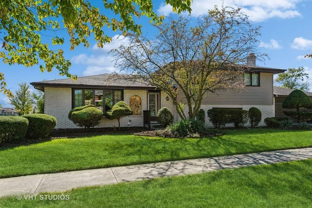 split level home featuring a front yard, brick siding, and a chimney