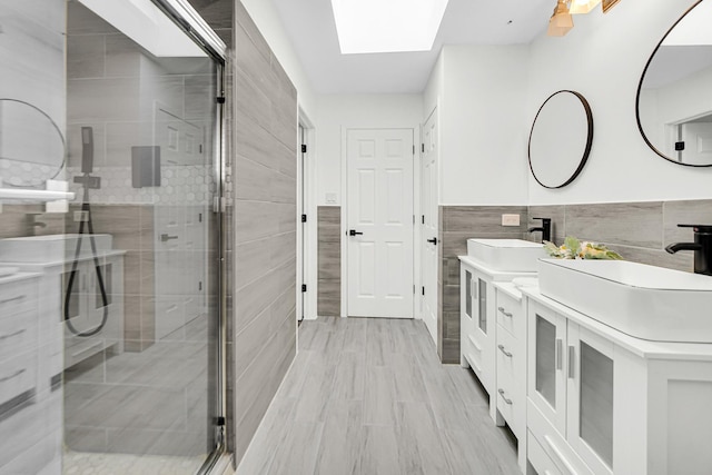 bathroom with tile walls, vanity, a shower with shower door, and a skylight