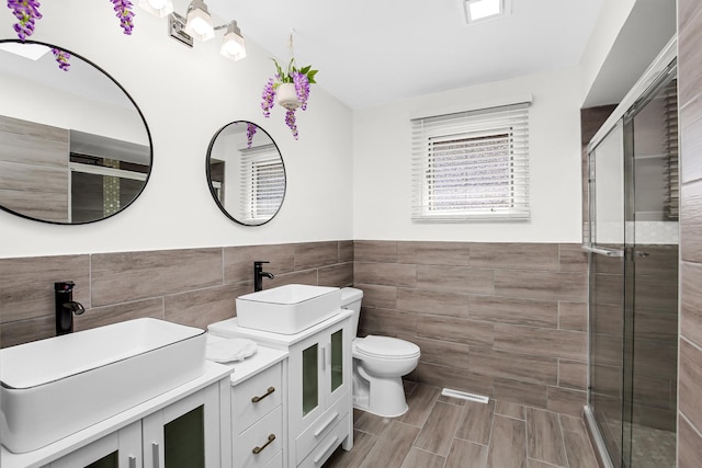 bathroom with toilet, a shower with shower door, tile walls, and vanity