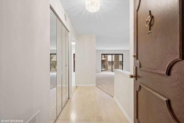 corridor featuring light wood finished floors, visible vents, baseboards, and a notable chandelier