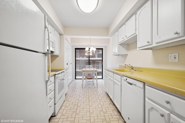 kitchen featuring white appliances, white cabinets, a sink, and a notable chandelier