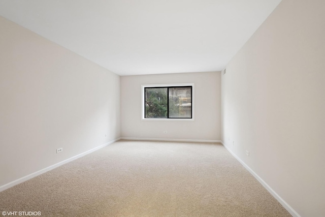 spare room with baseboards and light colored carpet