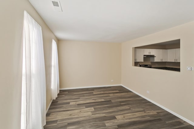 unfurnished room with dark wood-style floors, visible vents, and baseboards