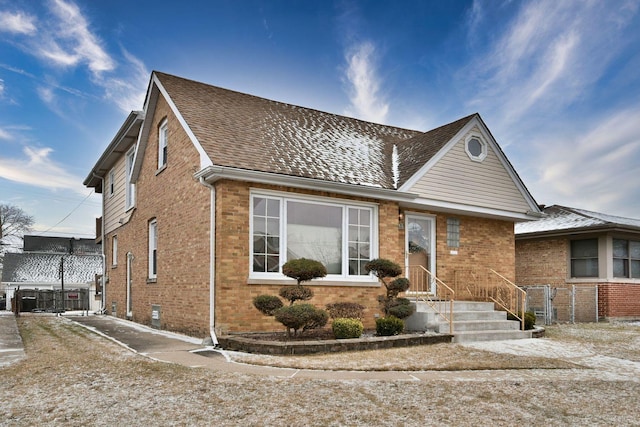 view of front of house featuring brick siding, a shingled roof, and fence