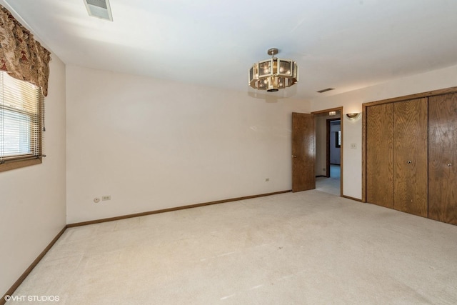 spare room featuring light carpet and an inviting chandelier