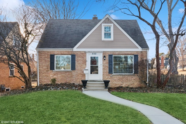 view of front facade with brick siding, a chimney, a front yard, and a shingled roof