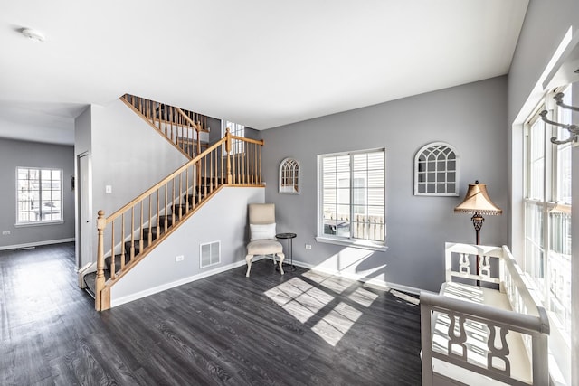 living area featuring dark wood-type flooring, a healthy amount of sunlight, visible vents, and baseboards