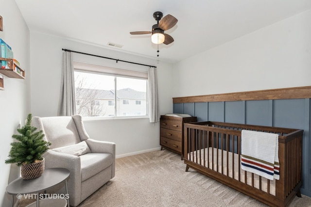 bedroom with a crib, baseboards, visible vents, a ceiling fan, and light colored carpet