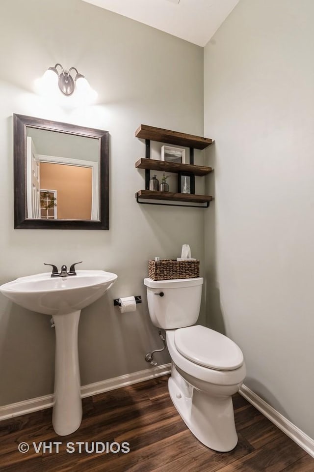 half bath featuring lofted ceiling, baseboards, toilet, and wood finished floors