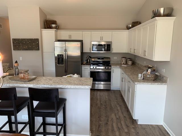 486 Ridge Ln, Bolingbrook, IL 60440 - kitchen featuring appliances with stainless steel finishes, white cabinetry, a breakfast bar area, light stone countertops, and dark wood-type flooring