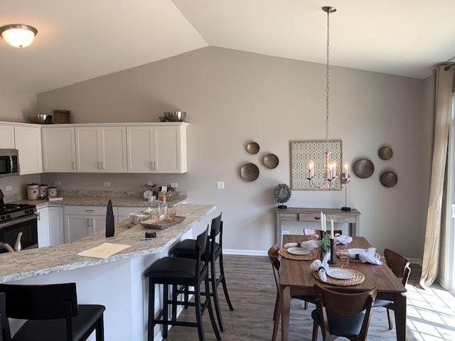 486 Ridge Ln, Bolingbrook, IL 60440 - kitchen with a kitchen bar, white cabinetry, vaulted ceiling, hanging light fixtures, and appliances with stainless steel finishes