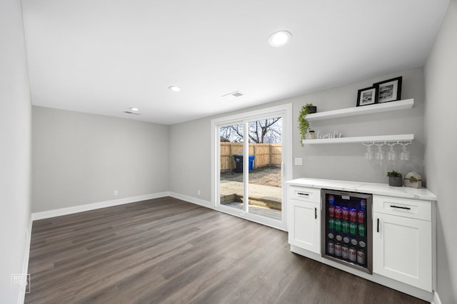 bar with wine cooler, dark hardwood / wood-style flooring, light stone counters, and white cabinets