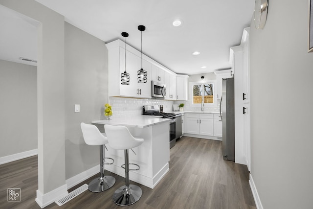 kitchen with pendant lighting, stainless steel appliances, white cabinets, a kitchen bar, and kitchen peninsula