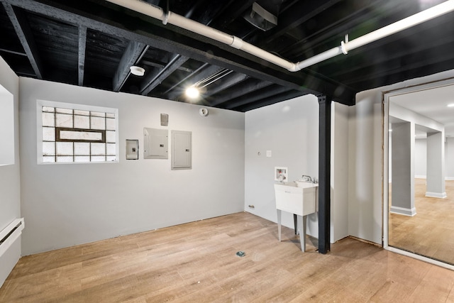 basement featuring a baseboard radiator, electric panel, and light hardwood / wood-style floors