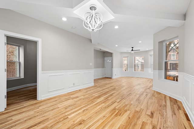 unfurnished living room with ceiling fan with notable chandelier and light hardwood / wood-style flooring