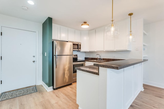 kitchen with a peninsula, a sink, appliances with stainless steel finishes, white cabinetry, and dark countertops