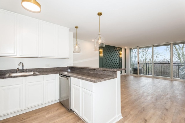 kitchen featuring a sink, dark countertops, a peninsula, white cabinets, and light wood finished floors