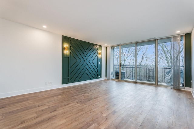 spare room featuring an accent wall, baseboards, expansive windows, recessed lighting, and light wood-style flooring