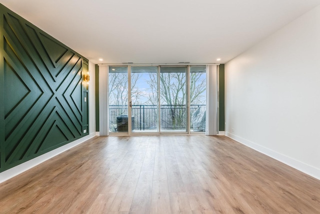 empty room featuring recessed lighting, expansive windows, baseboards, and light wood-style flooring