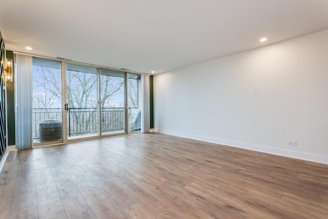 empty room with recessed lighting, wood finished floors, baseboards, and expansive windows