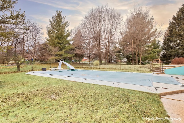 view of swimming pool with a water slide, a lawn, fence, and a fenced in pool