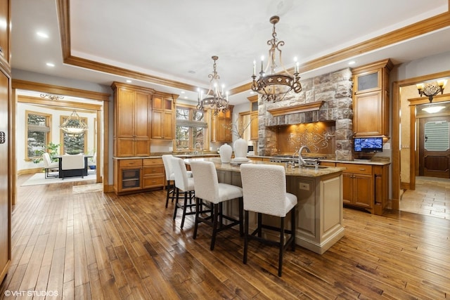 kitchen with a kitchen bar, wood-type flooring, hanging light fixtures, a tray ceiling, and a kitchen island with sink