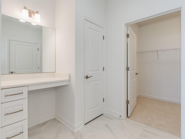 bathroom with marble finish floor, baseboards, a walk in closet, and vanity