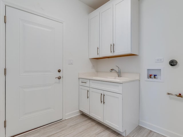 washroom featuring hookup for a washing machine, cabinet space, light wood-style floors, a sink, and baseboards