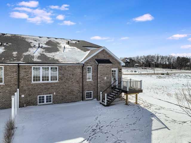 snow covered back of property featuring stairs, a deck, and brick siding