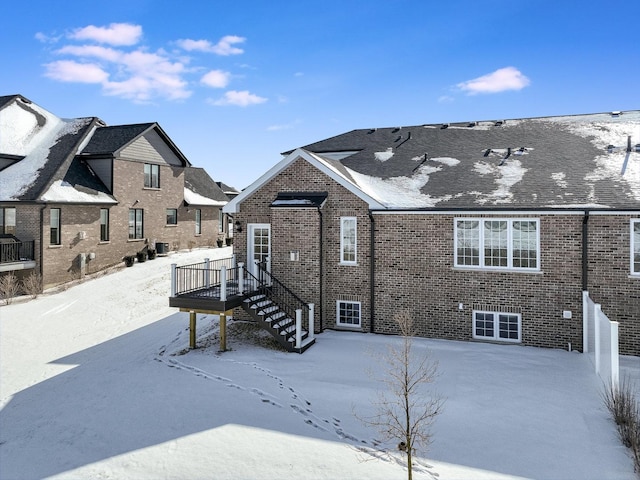 snow covered property featuring a wooden deck, stairs, and brick siding