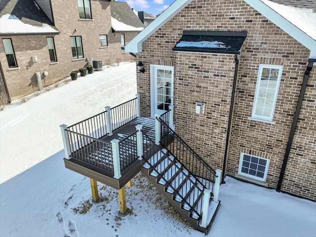 snow covered property entrance featuring brick siding and central air condition unit