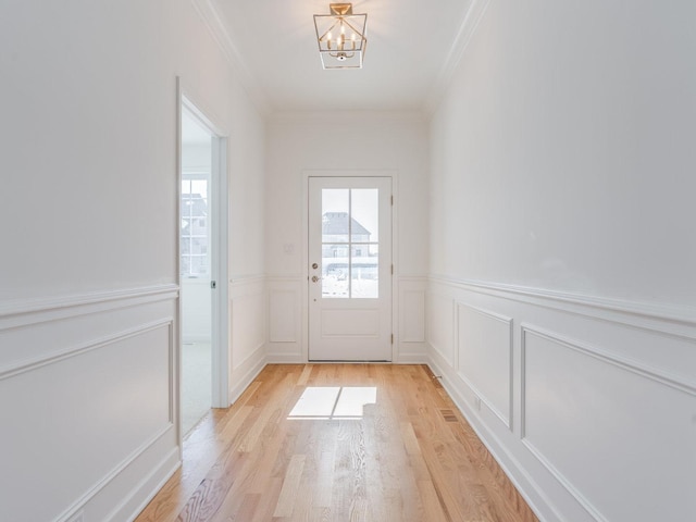 doorway featuring a wainscoted wall, crown molding, light wood finished floors, and an inviting chandelier