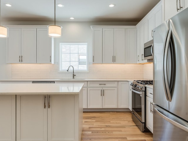 kitchen with a sink, stainless steel appliances, light countertops, and decorative light fixtures