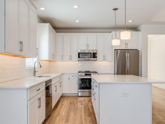 kitchen featuring stainless steel appliances, light countertops, hanging light fixtures, white cabinetry, and a sink