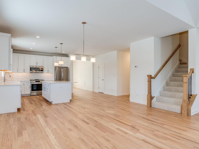 kitchen with decorative light fixtures, light countertops, appliances with stainless steel finishes, open floor plan, and a kitchen island