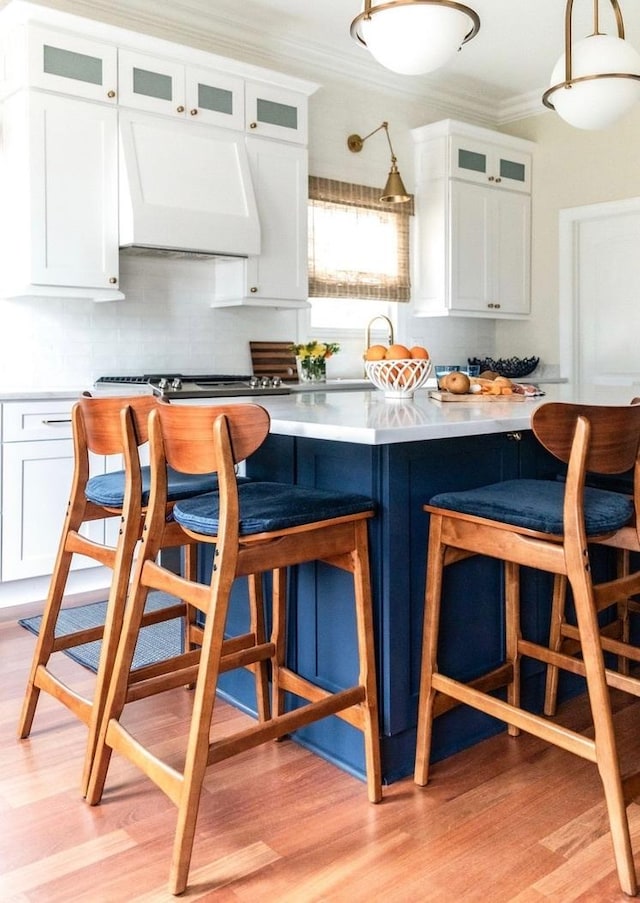 kitchen with a breakfast bar area, light countertops, ornamental molding, white cabinets, and exhaust hood