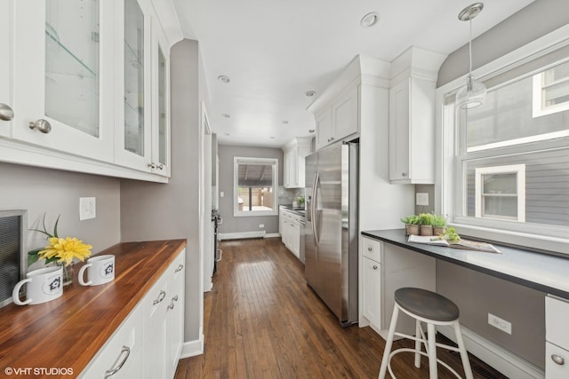 kitchen with dark wood-type flooring, stainless steel fridge, wooden counters, hanging light fixtures, and white cabinets