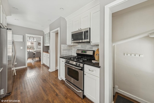 kitchen with dark wood-type flooring, white cabinets, appliances with stainless steel finishes, a notable chandelier, and backsplash