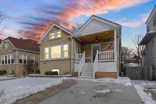 bungalow-style home featuring a porch, brick siding, fence, a ceiling fan, and stairway