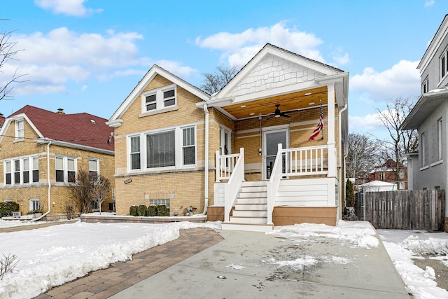 bungalow featuring ceiling fan, a porch, brick siding, fence, and stairs