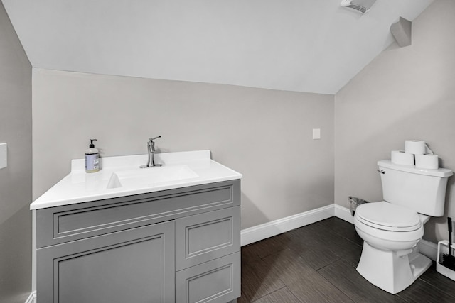 half bath with toilet, vaulted ceiling, vanity, wood finished floors, and baseboards