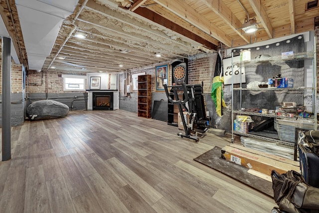 unfurnished living room featuring a fireplace, brick wall, and wood finished floors