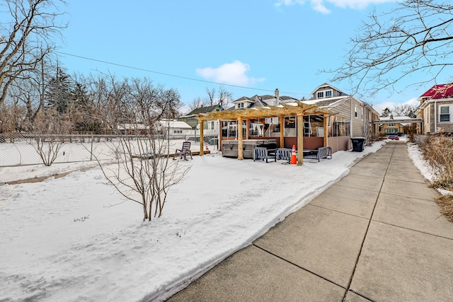 snow covered back of property with a jacuzzi, fence, and a pergola