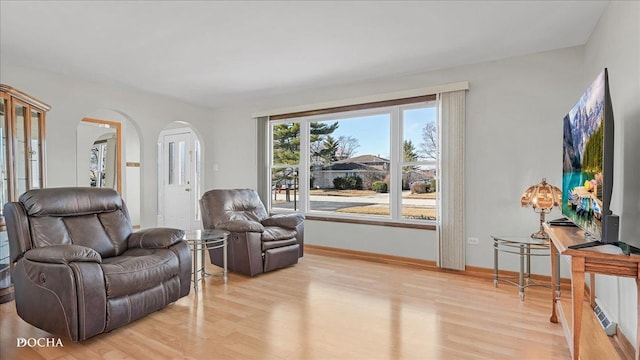 living area featuring light wood-type flooring, arched walkways, and baseboards