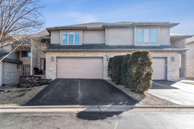 view of front facade featuring a shingled roof, brick siding, driveway, and an attached garage