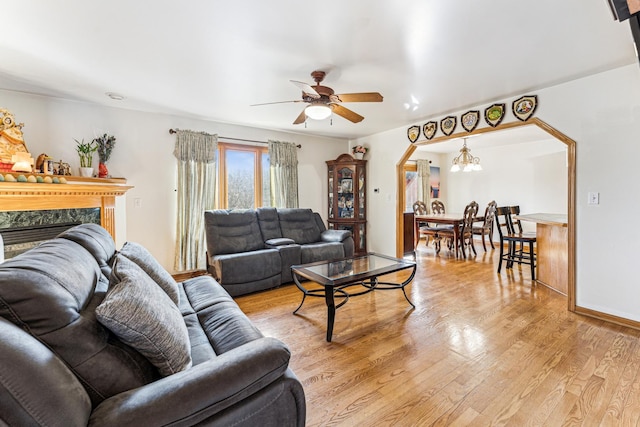 living room with arched walkways, light wood finished floors, a high end fireplace, baseboards, and ceiling fan with notable chandelier